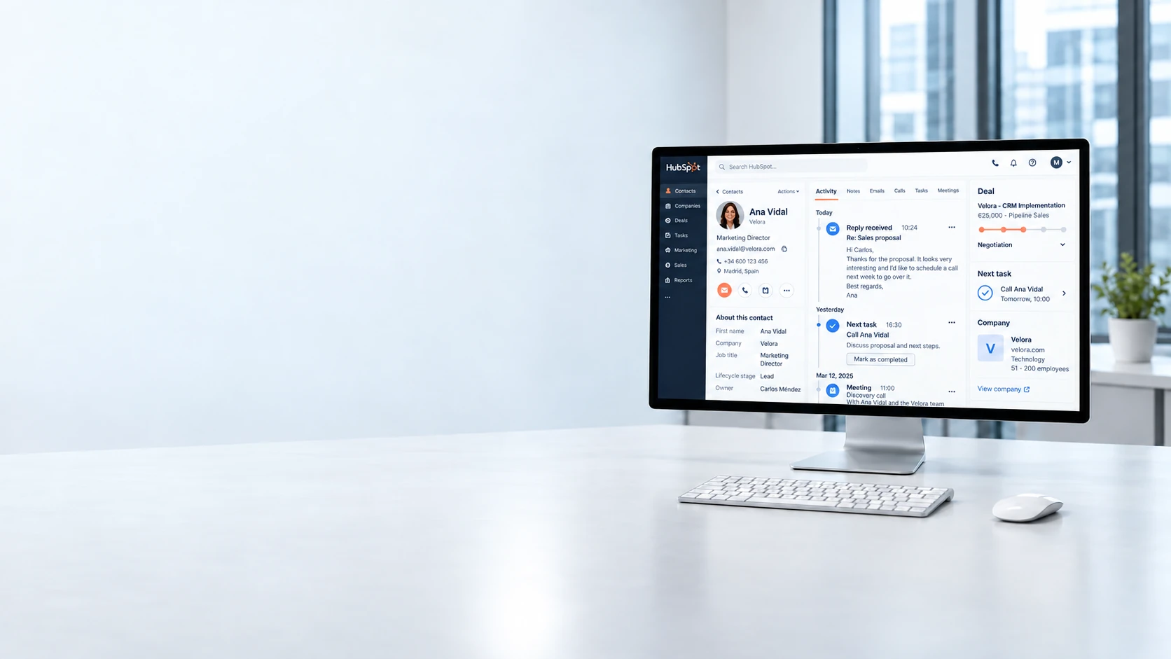 Workstation with a monitor, keyboard and mouse, showing an illustrative HubSpot contact record on screen